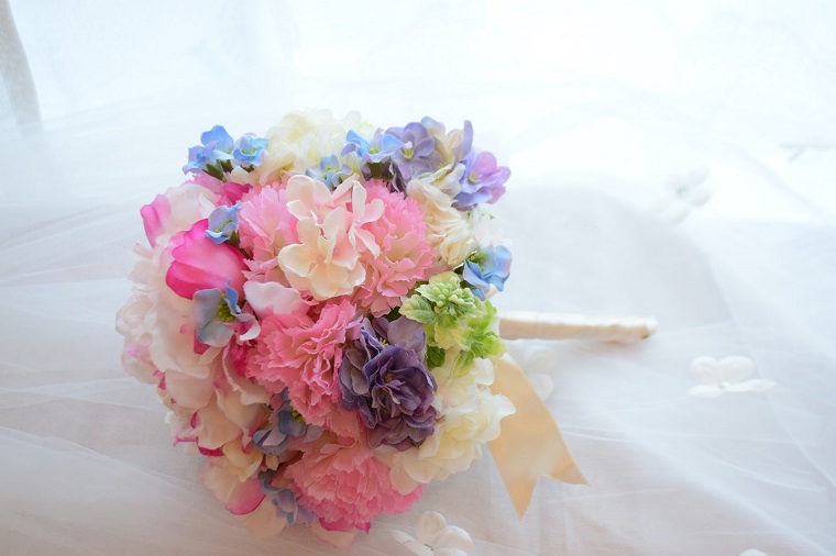 ピンクホワイトパープルブルーなどのパステルカラーの造花でラウンド形のウエディングブーケ